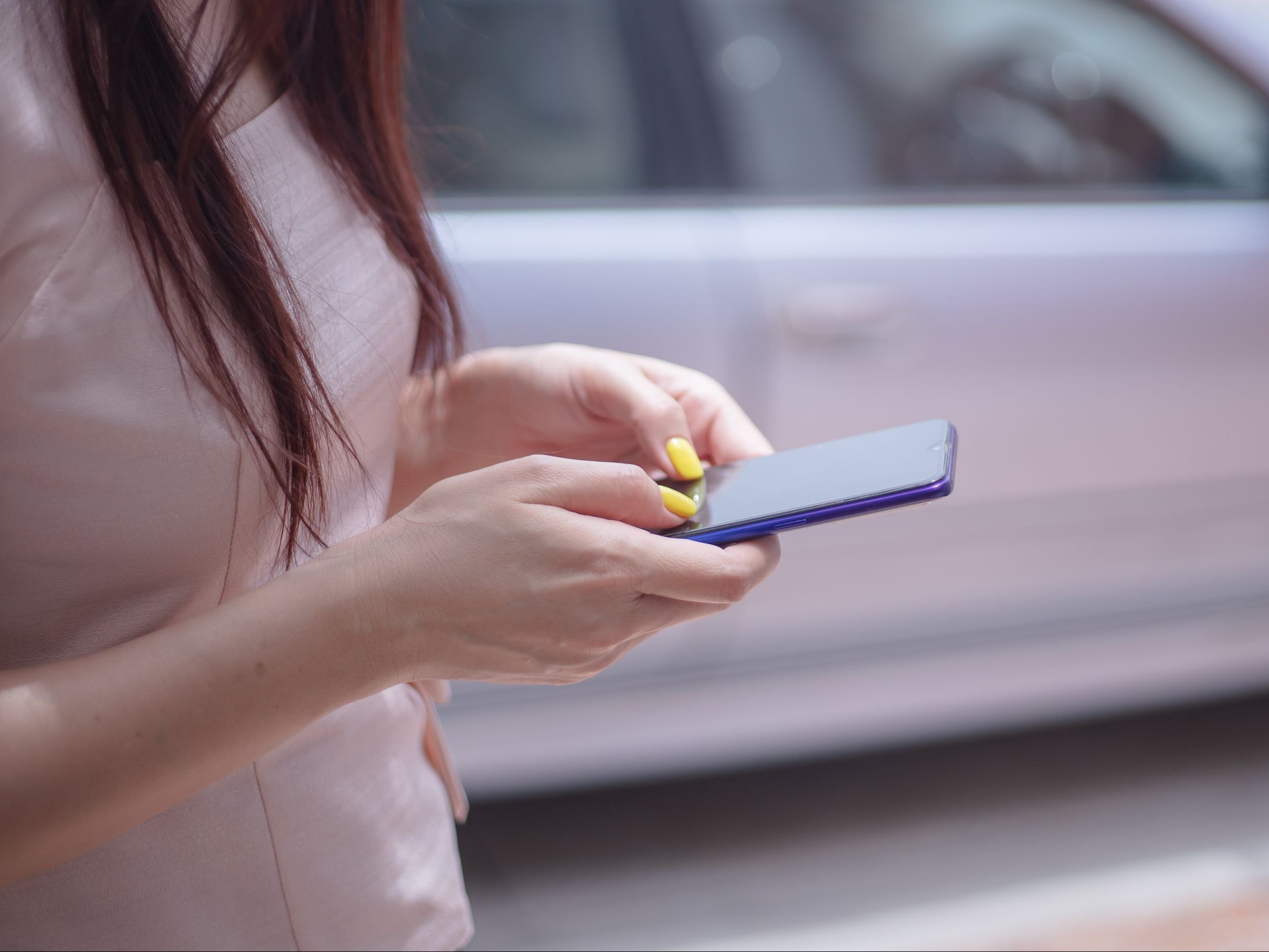 Customer using her smartphone beside a parked car