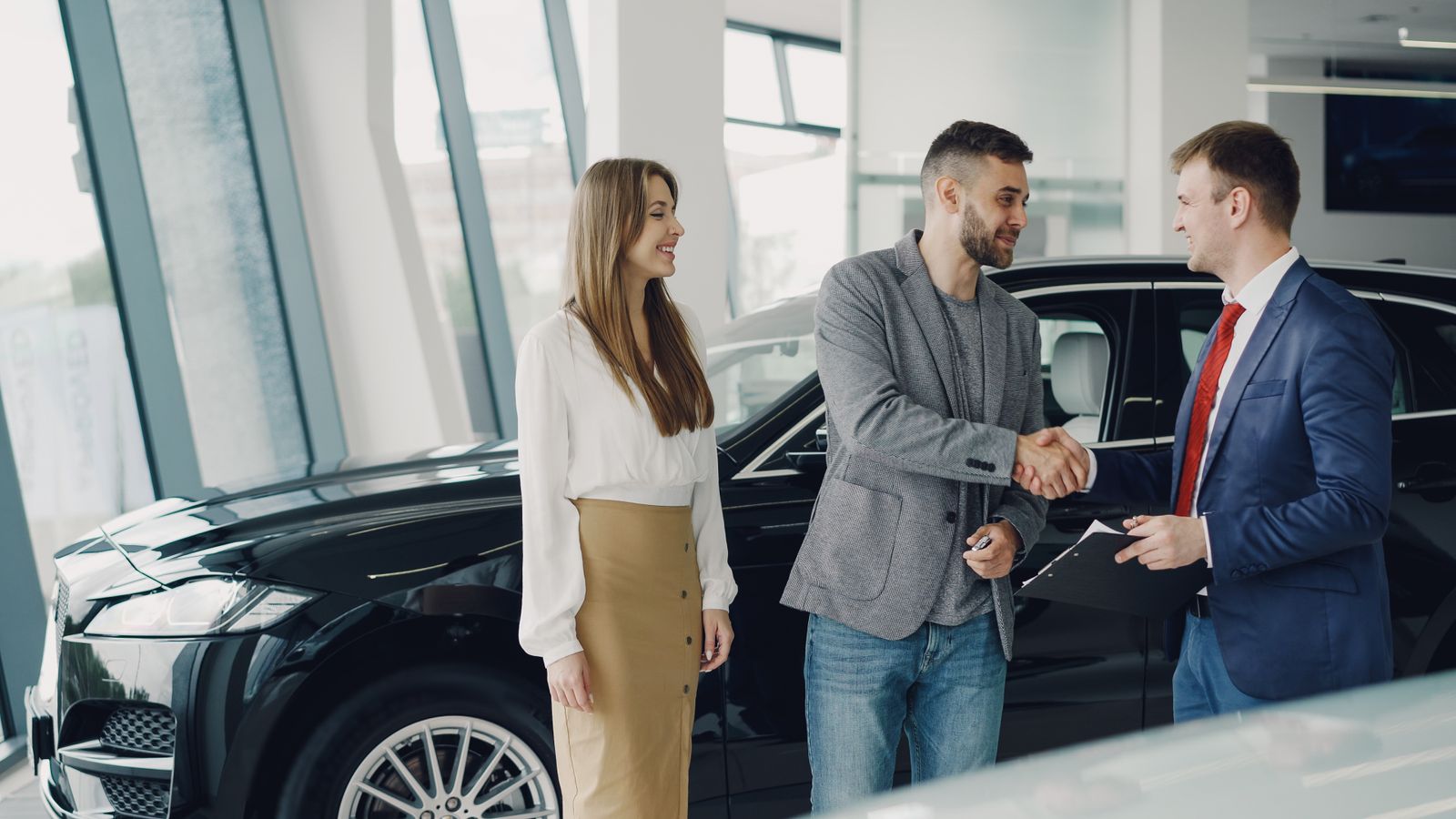 Car dealer shaking hands with customers beside a new car in a bright showroom