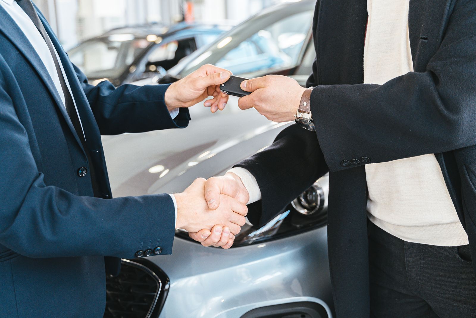 Salesperson handing car keys to a customer and shaking hands in a dealership showroom